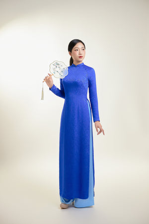 Full-length Thai Tuan silk brocade Ao Dai in blue with intricate leaf pattern.
