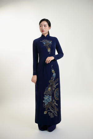Elegant woman in a traditional hand-beaded Ao Dai featuring intricate lotus designs on a navy background.