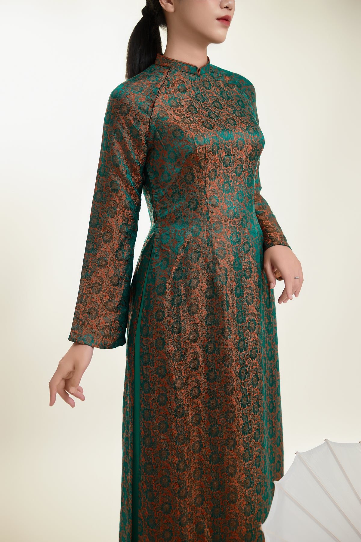 Close-up of a luxurious green and gold silk Ao Dai showcasing detailed patterns.
