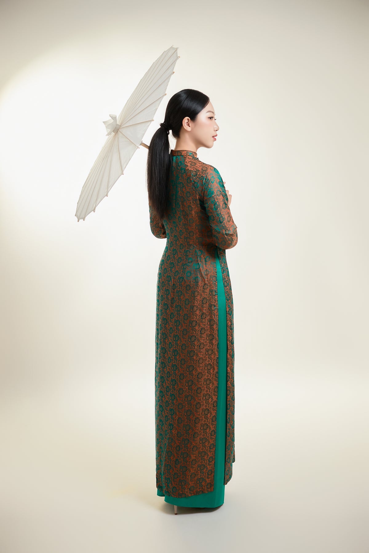 Back view of a traditional green and gold silk Ao Dai with flowing design.