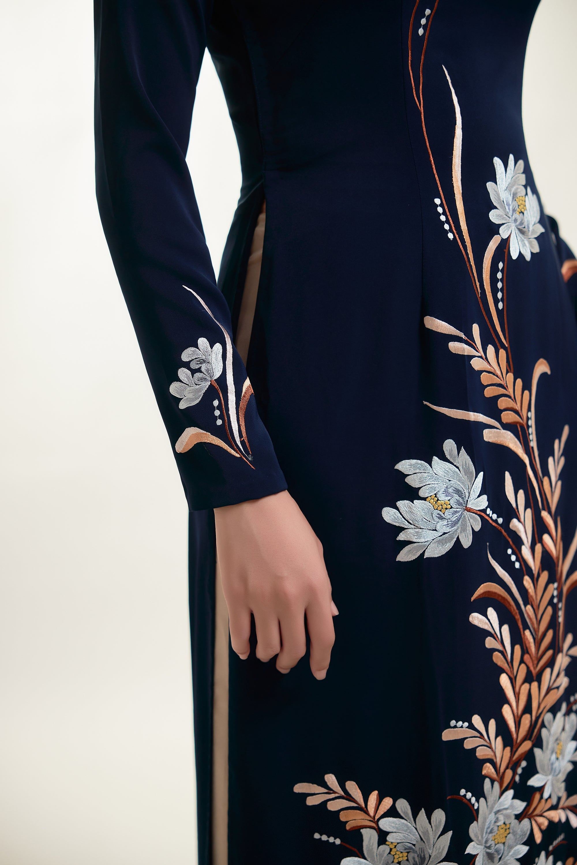 Close-up of embroidered chrysanthemums on dark blue silk Ao Dai garment, showcasing intricate design and elegance.