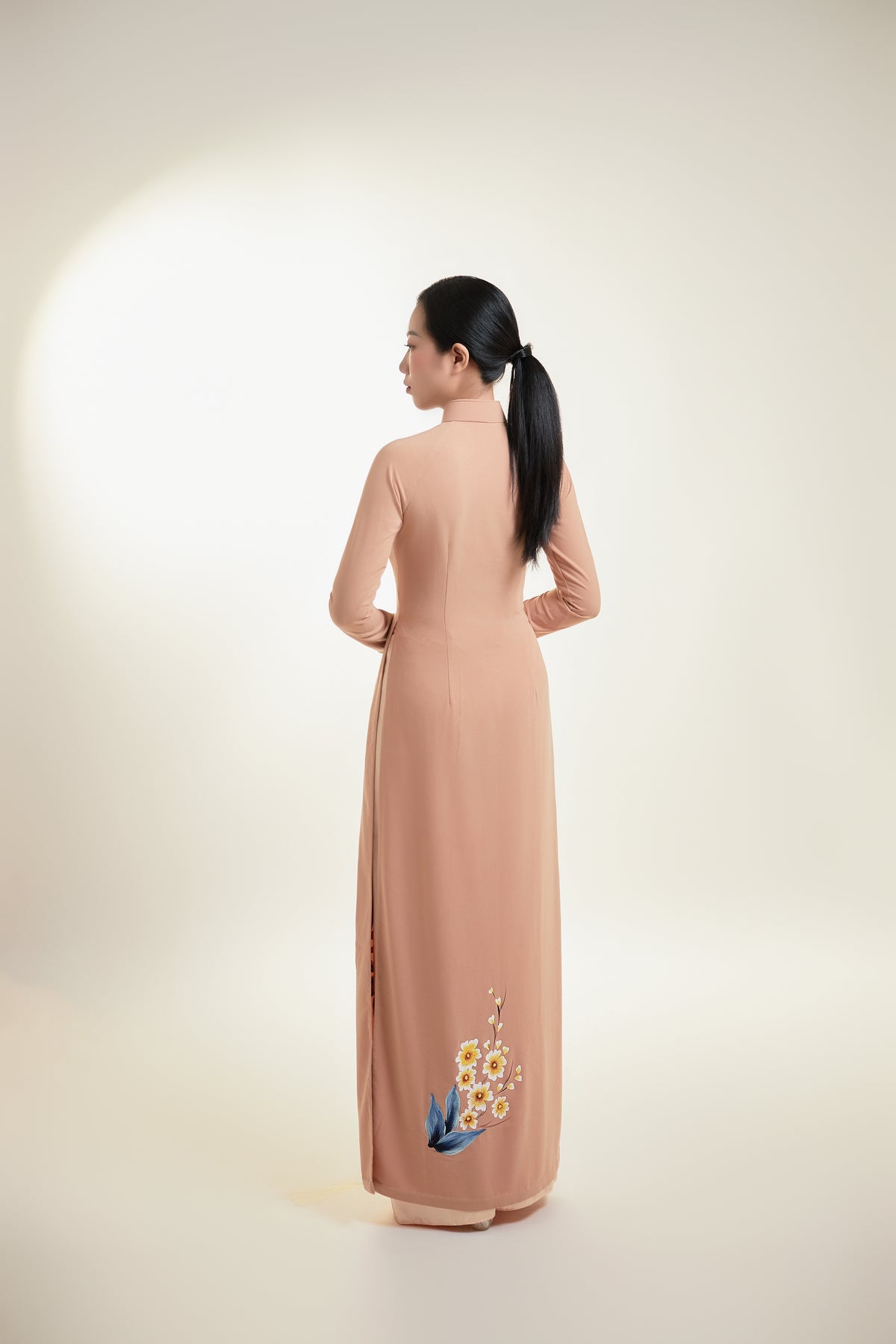 Hand-painted Ao Dai on nude pink silk, showcasing intricate floral design and elegant silhouette from the back.