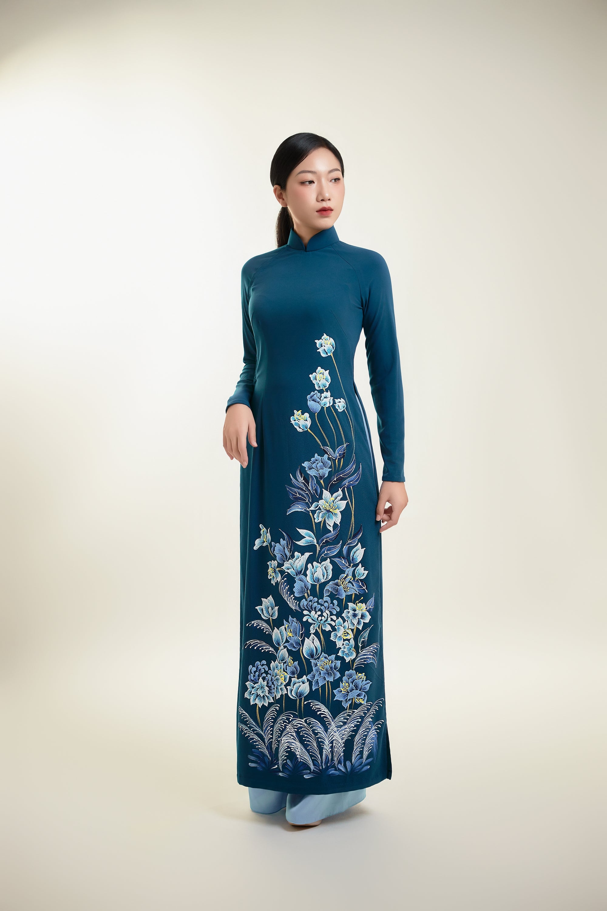 Hand-painted ao dai on teal silk featuring intricate floral designs, showcasing traditional Vietnamese elegance.