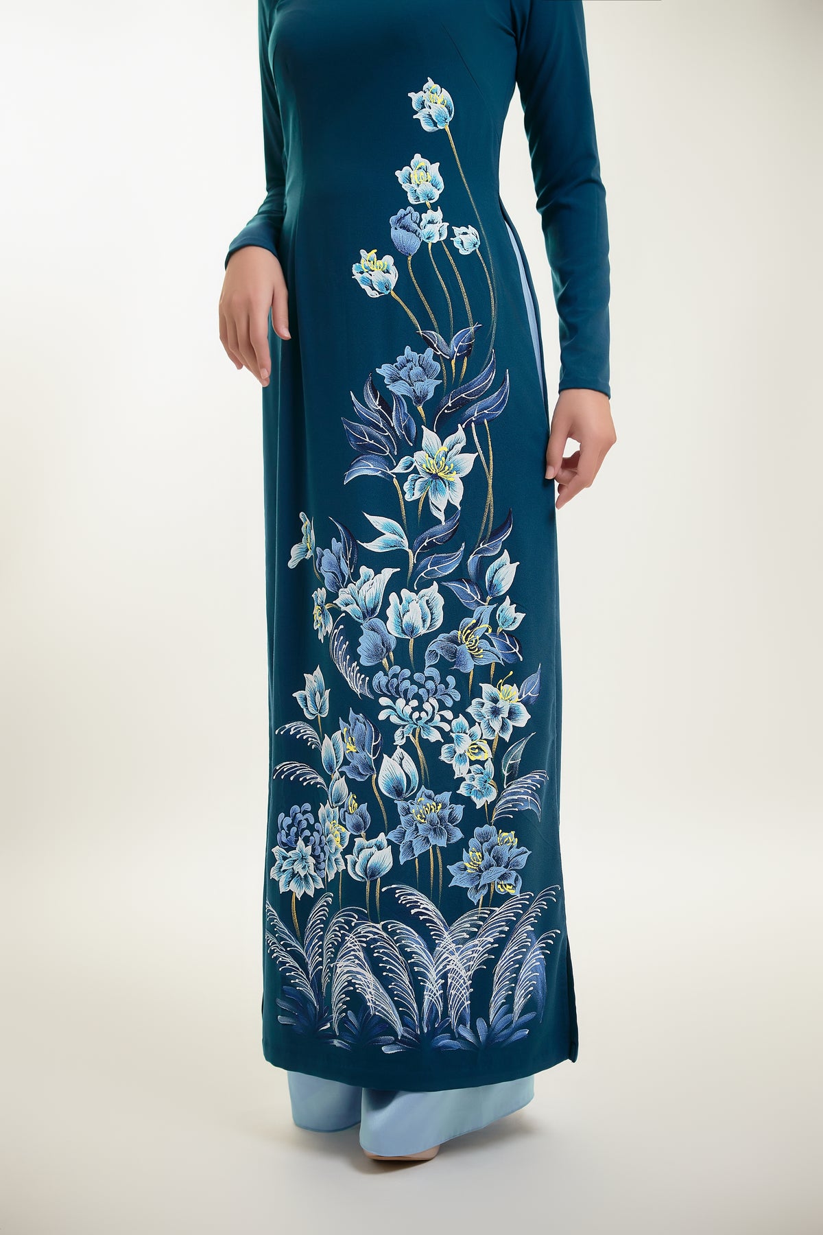 Hand-painted ao dai on teal silk featuring intricate floral designs, showcasing traditional Vietnamese elegance.