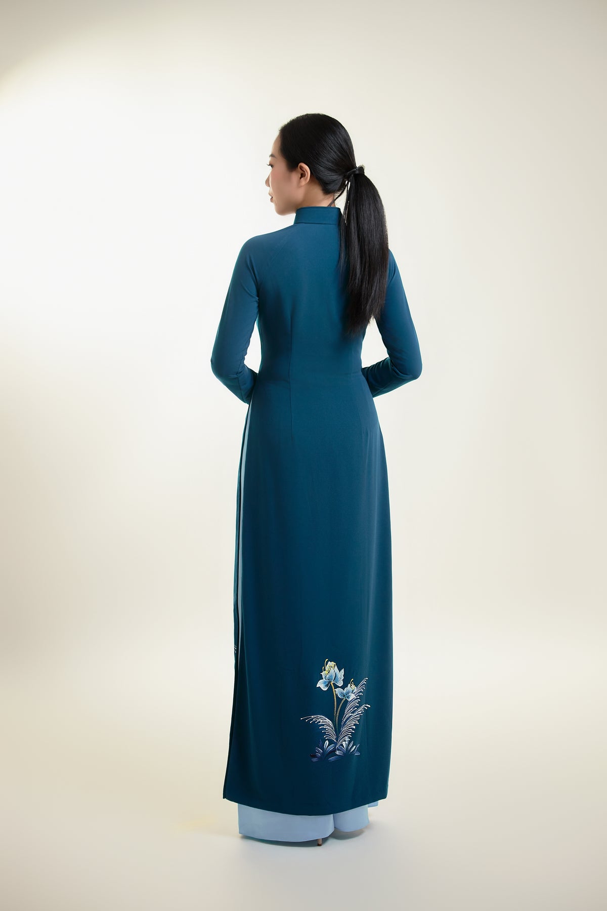 Hand-painted ao dai on teal silk, showcasing intricate design and elegant silhouette from the back.
