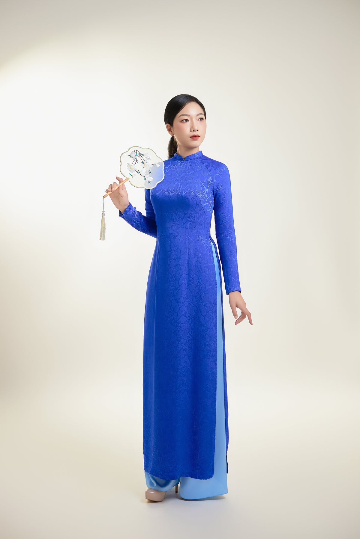 Full-length Thai Tuan silk brocade Ao Dai in blue with intricate leaf pattern.