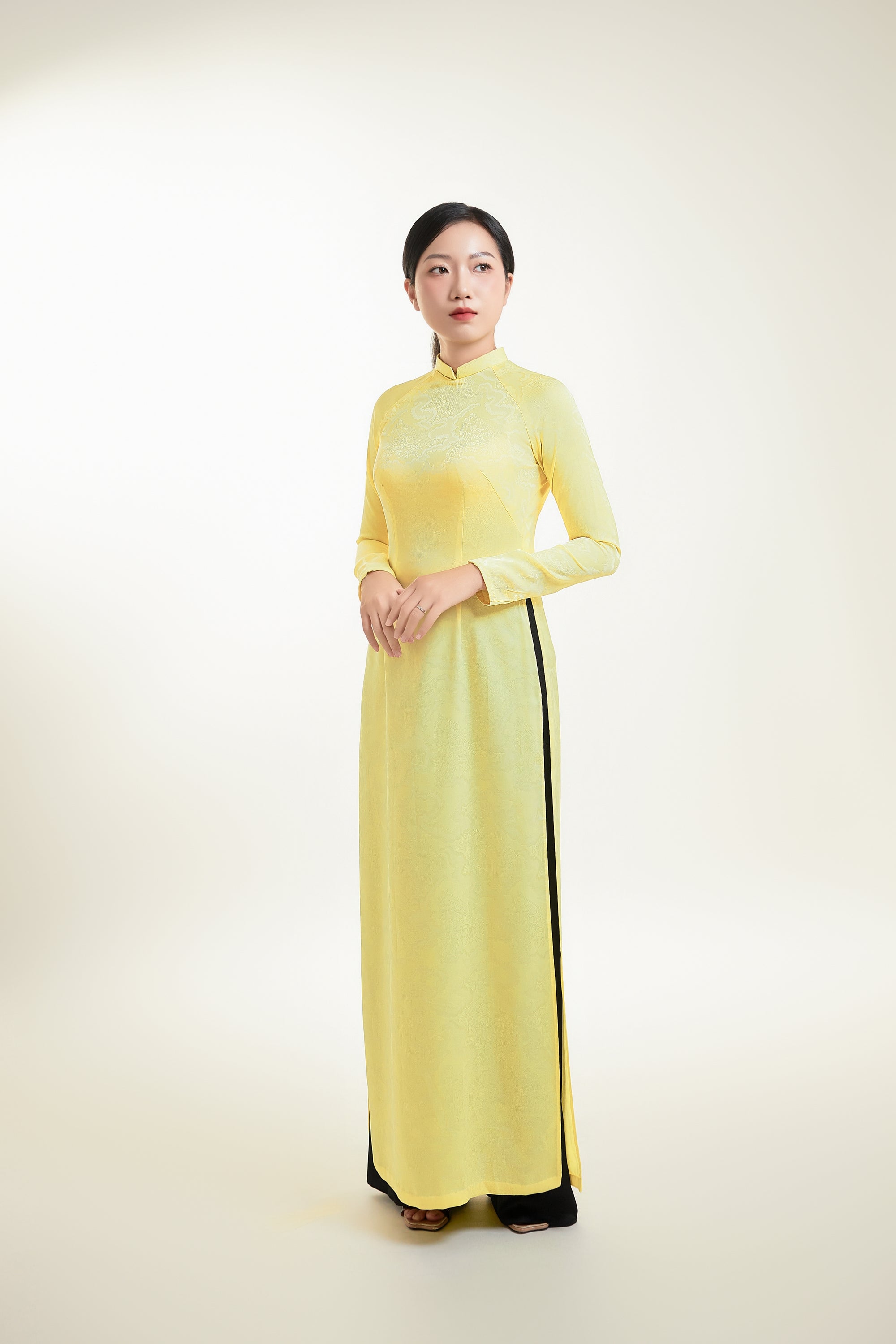 Elegant pale yellow silk brocade Ao Dai with intricate patterns, front view.