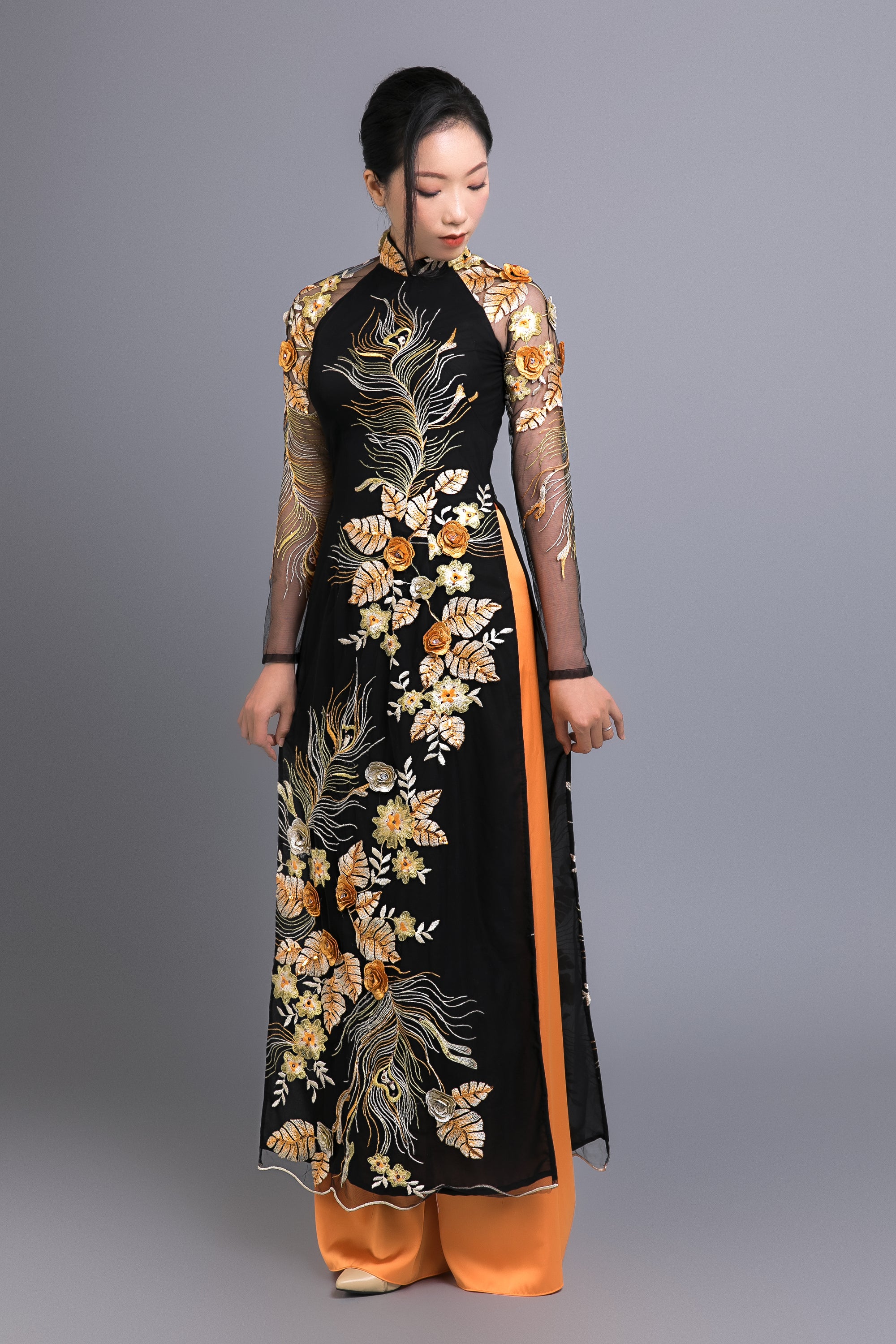 Custom black chiffon ao dai with floral and peacock lace details, paired with orange pants for a traditional Vietnamese look.